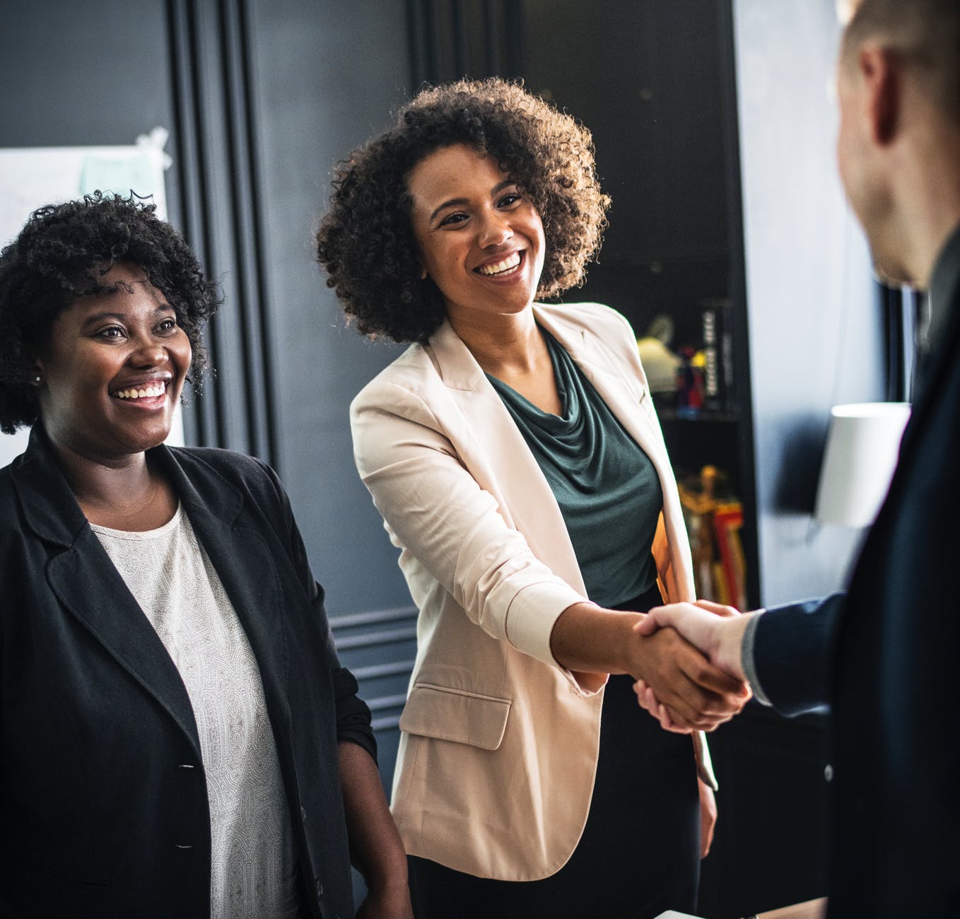 woman wears beige suit hand shaking man wear suit